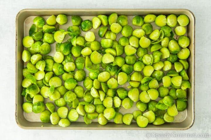 Single layer of brussels sprouts laid on a baking tray.