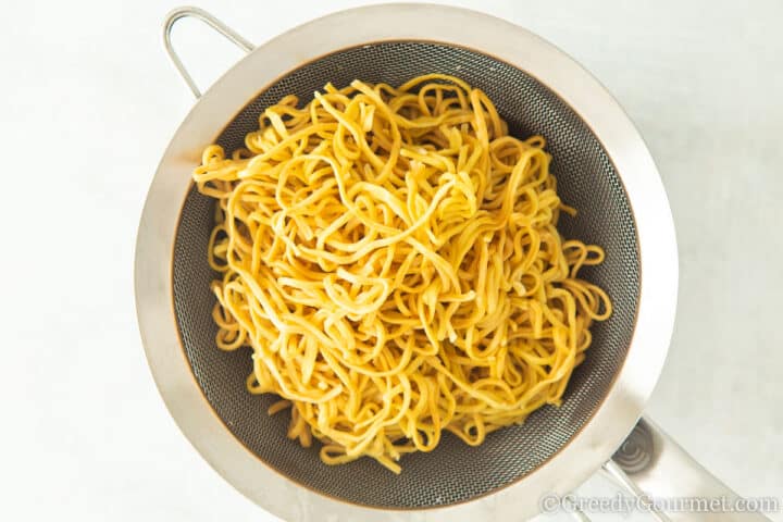 straining cooked egg noodles.