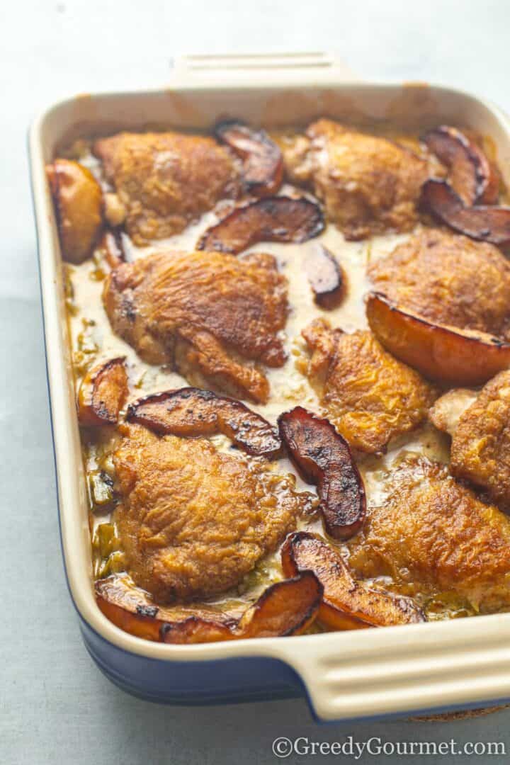 Golden baked Normandy chicken in a casserole dish sprinkled with herbs.