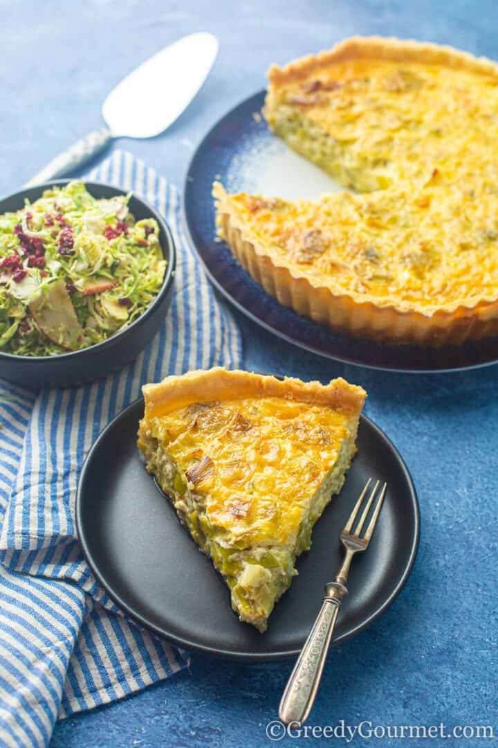 Slice of Leek tart on a plate with a bowl of salad. 