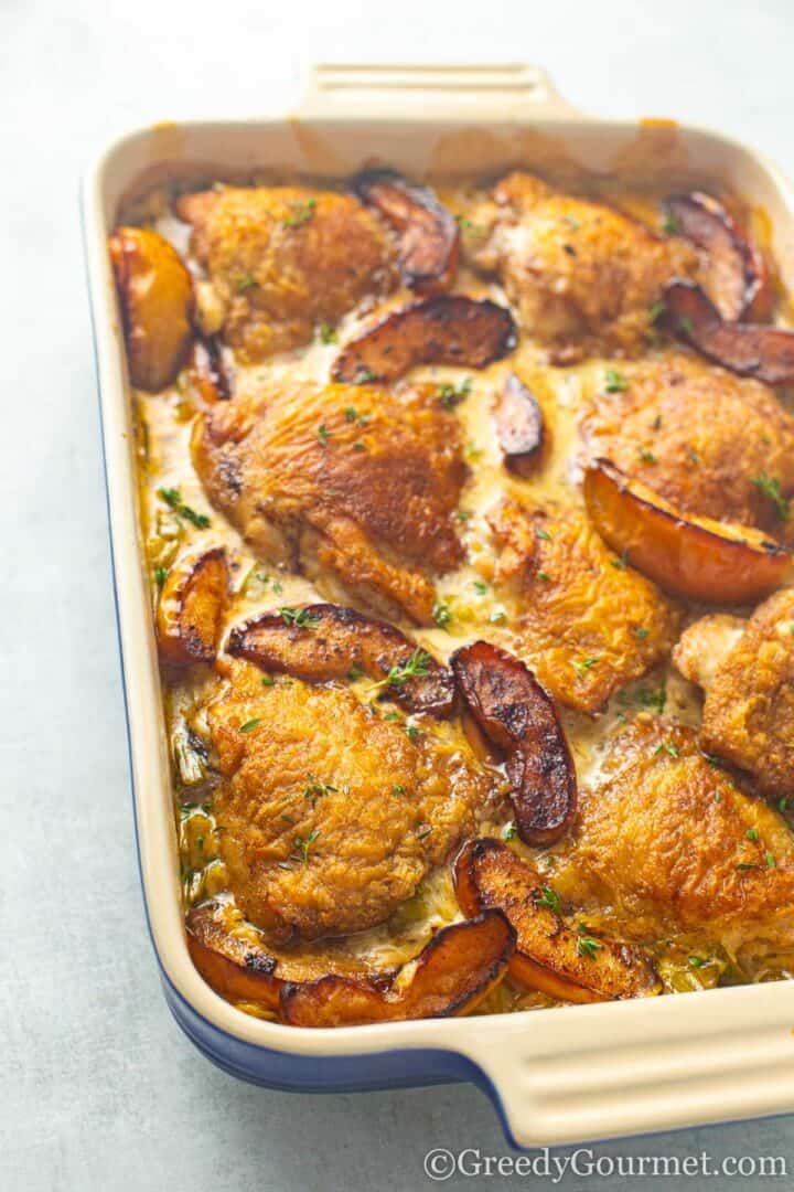 Golden baked Normandy chicken in a casserole dish sprinkled with herbs.