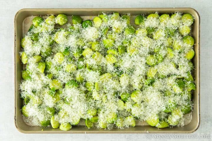 Grated parmesan cheese sprinkled on top of raw brussels sprouts.