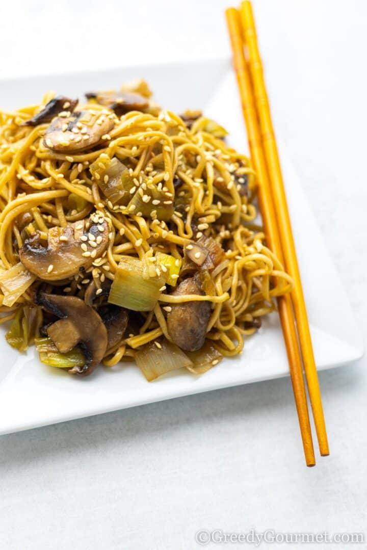 leek and mushroom noodles served on a white plate with chopsticks.