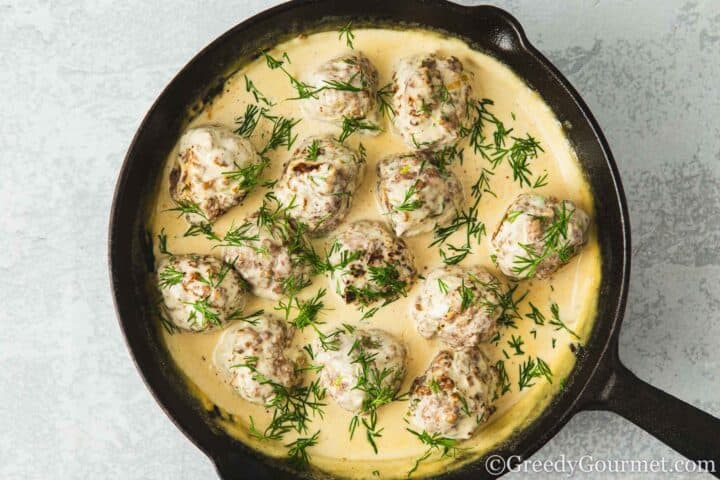Lamb meatballs in sauce sprinkled with dill in a pan.