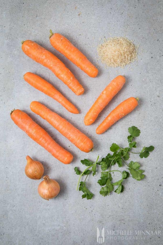 Ingredients for carrot soup on a grey counter top Coriander Carrots onions rice