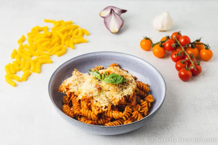 pasta bake in a bowl with fresh tomatoes next to it.