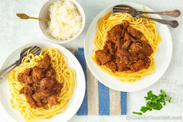 Beef Pastitsada being served with herbs and grated cheese.