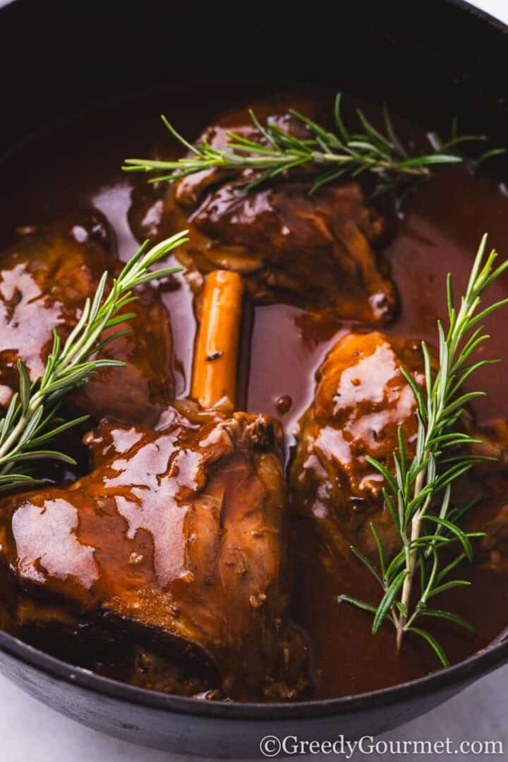cooked lamb shanks in a pot with fresh herbs.