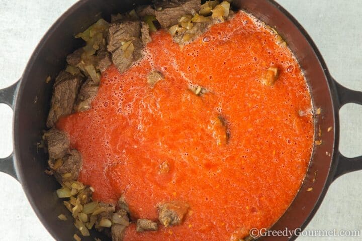 Adding pureed canned tomatoes to braised beef and onions.