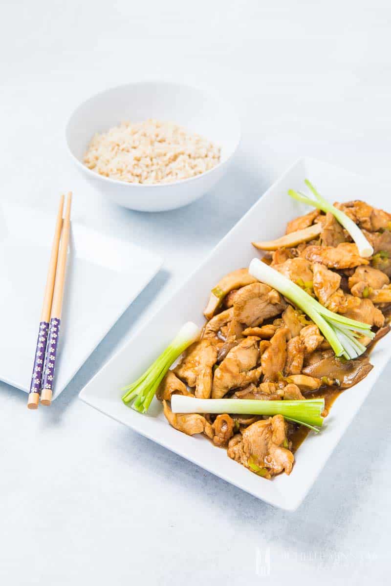 A plate of chicken in oyster sauce and a bowl of rice and chopsticks 