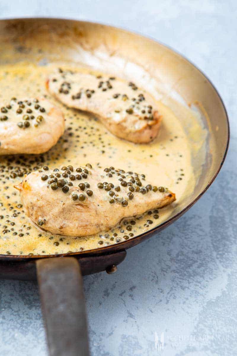 Three chicken breasts in a saute pan with peppercorns 