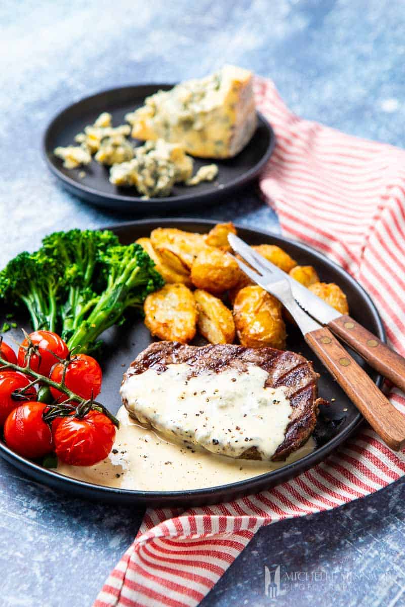 A plate of steak and potatoes with a blue cheese sauce