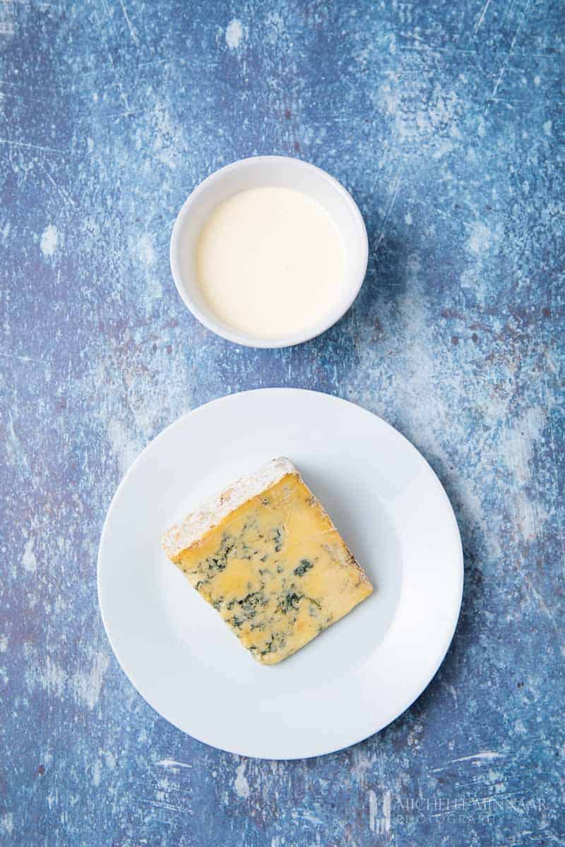 A block of blue cheese and a bowl of blue cheese sauce