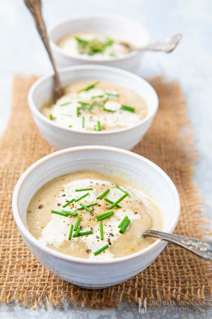 Three bowls filled with Jerusalem artichoke Soup with spoons in them.