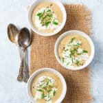 Three bowlfuls of Sunchoke Soup with three spoons on grey background.