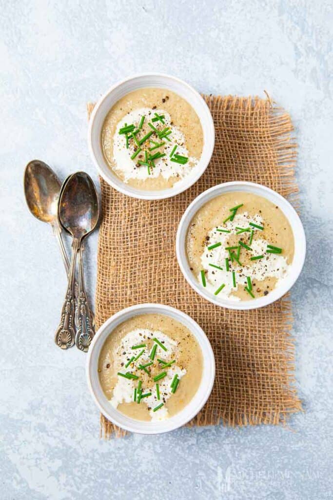 Three bowlfuls of Sunchoke Soup with three spoons on grey background.