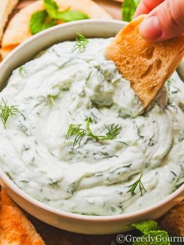 a person dipping a cracker into a bowl of creamy dip