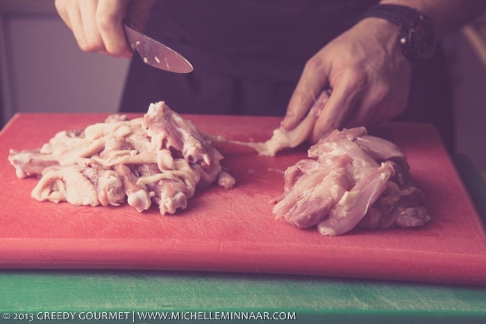 Someone cutting up raw chicken on a cutting board