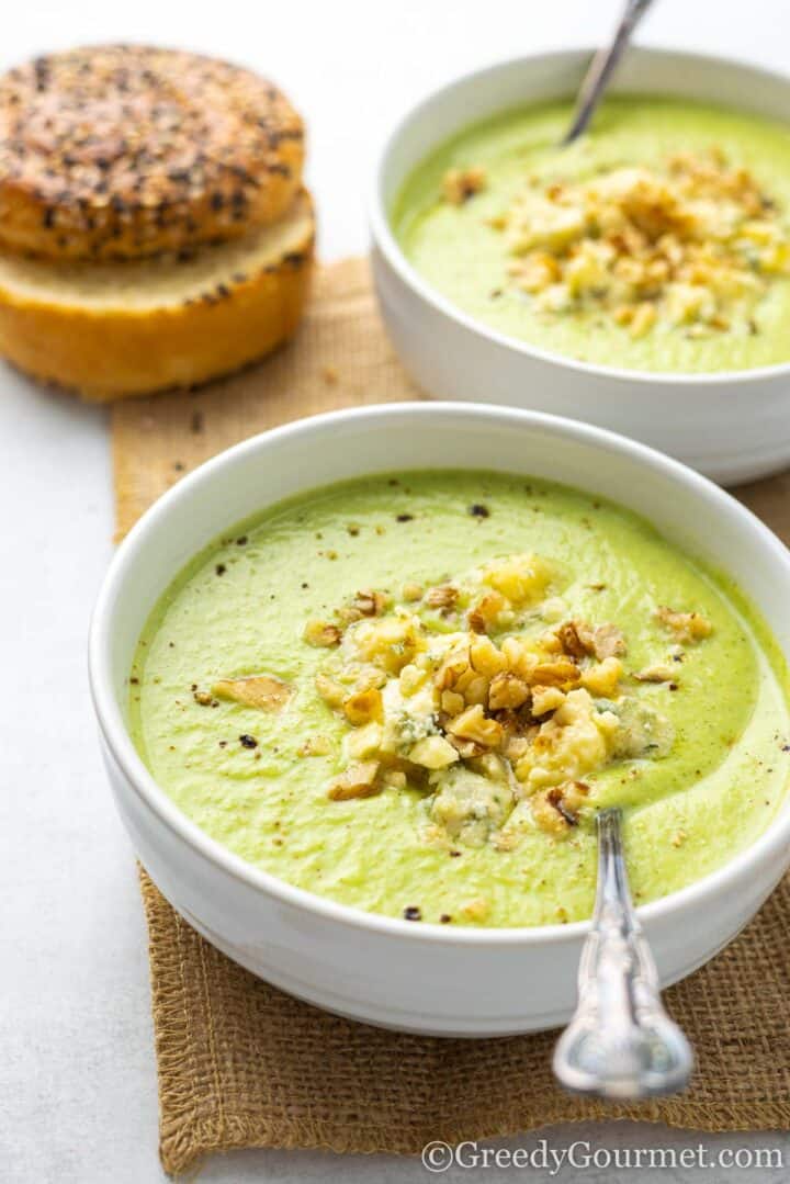 broccoli and stilton soup in a bowl with a spoon and bagel.