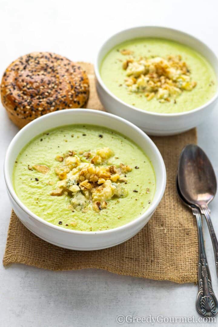 broccoli and stilton soup in a bowl with a spoon and bagel.
