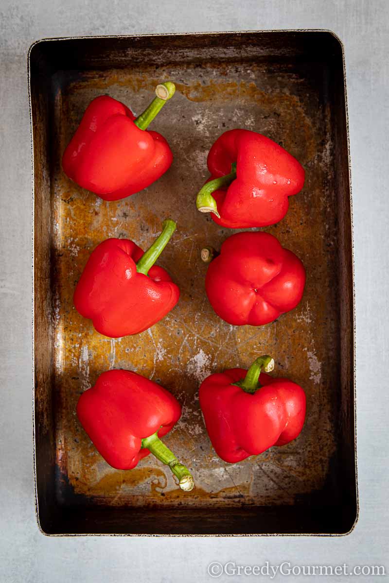Six red peppers about to be roasted in a pan