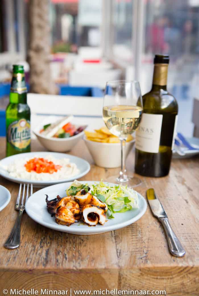 A plate of grilled calamari, hummus and a glass of white wine