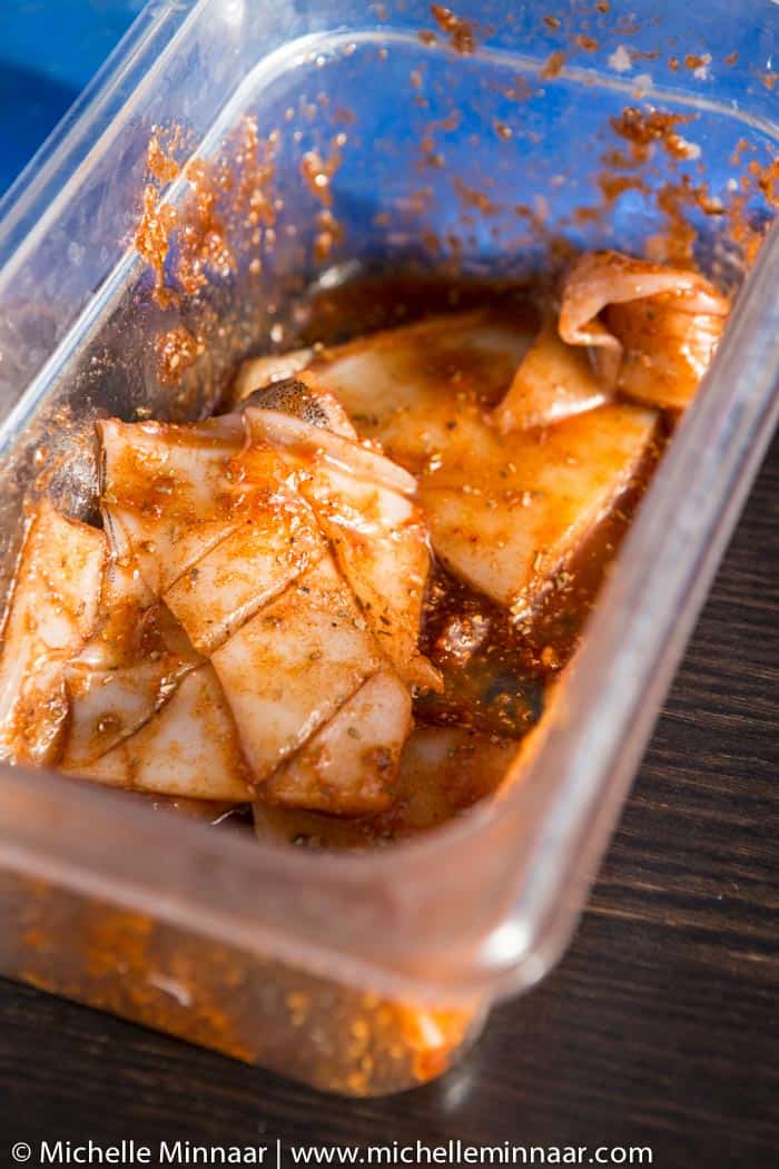 Raw marinated kalamari in a plastic bowl