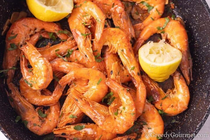 Pan fried garlic butter prawns with a slice of lemon in a cooking pan.