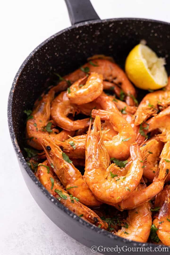 Pan fried garlic butter prawns with a slice of lemon in a cooking pan.