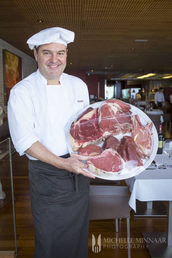 A chef holding a plate of a variety of steaks