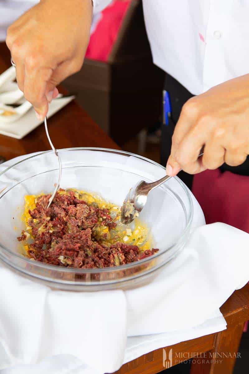 Steak tartare being prepared table side in a glass bowl 