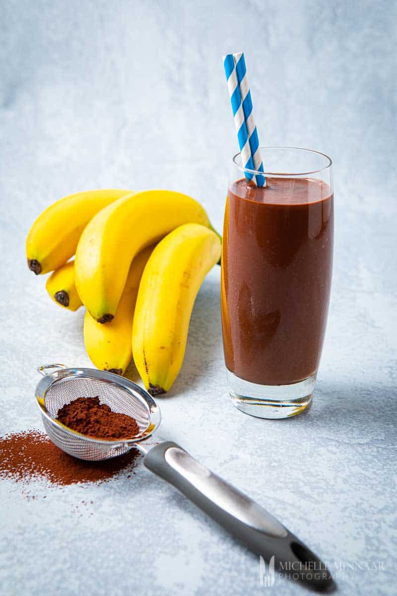 Almond Milk Protein Shake with cocoa powder and fresh banana bunch.