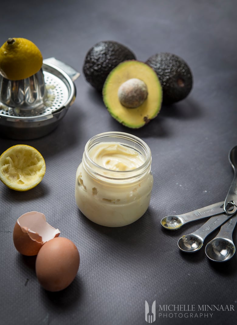 A clear jar of avocado oil mayo, an egg, avocado and a lemon 