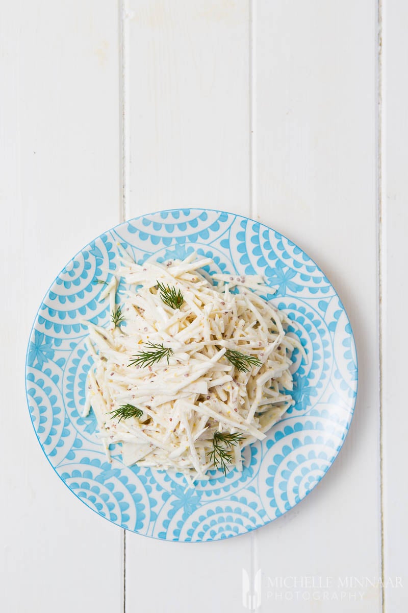 A plate of celeriac remoulade : white strips of celeriac on a blue plate in a white sauce