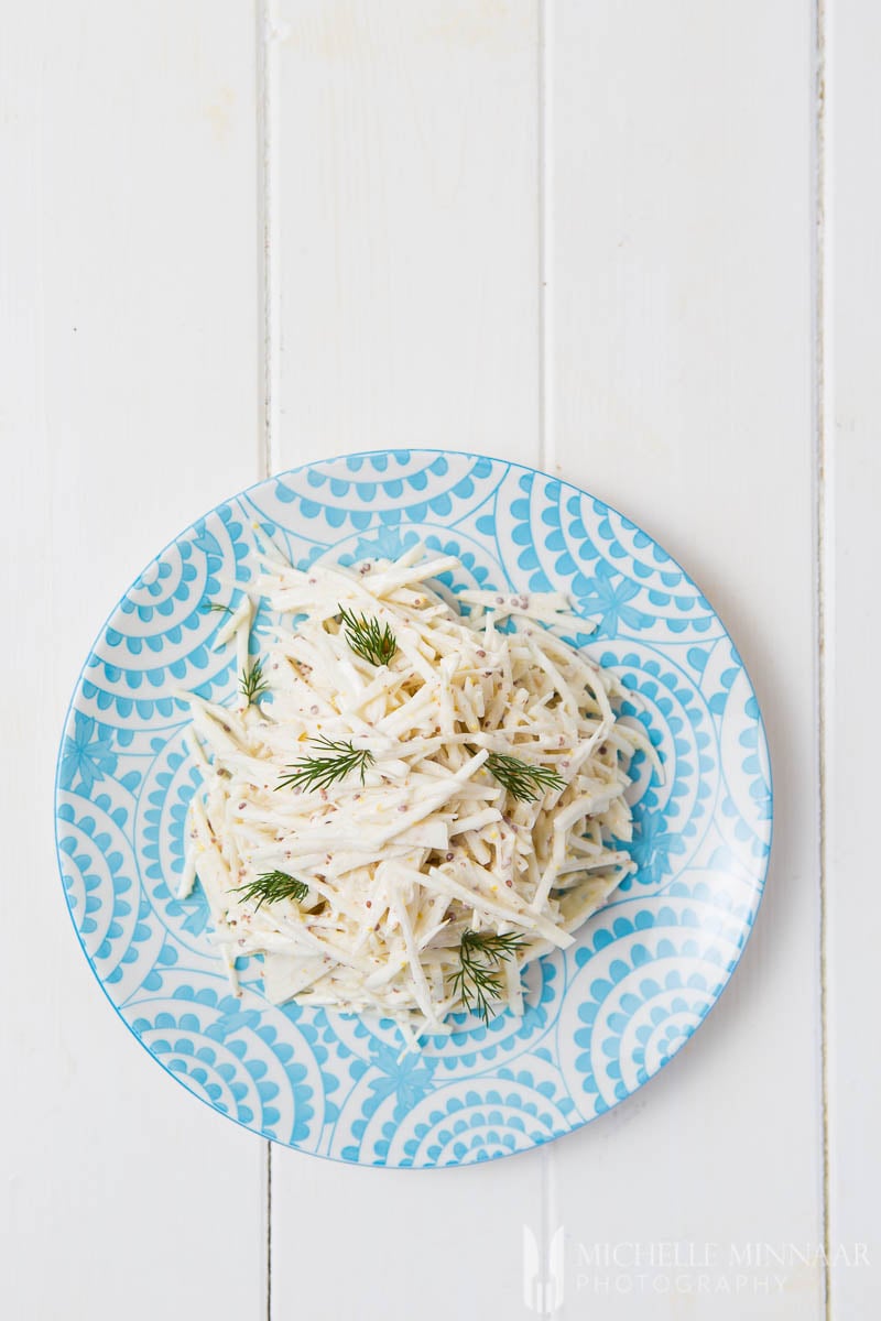 A plate of celeriac remoulade : white strips of celeriac on a blue plate in a white sauce 