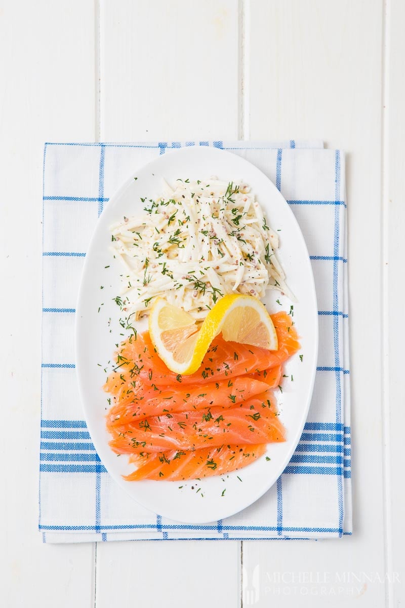 A plate of smoked salmon with a lemon on top next to celeriac remoulade