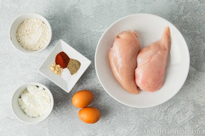 Chicken, flour, egg and spices on a table.