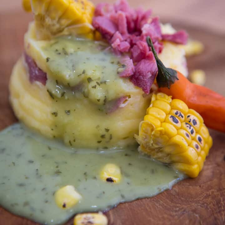 Costilla con Papa Encausada - pork potatoes corn and green sauce on a cutting board