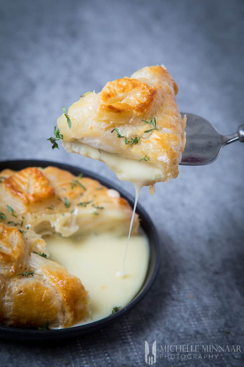 Camembert en Croute - a cheesy slice being cut from a wheel in a black dish