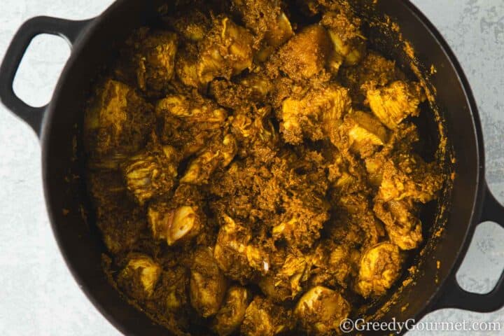 Browned chicken in a pan with korma paste.