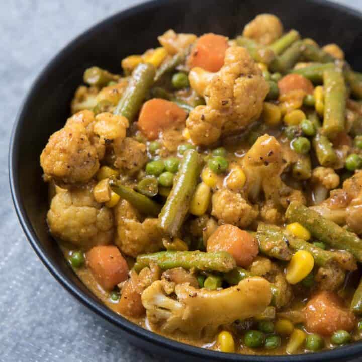 A bowl of vegetarian korma, cauliflower, green beans, corns in a orange sauce