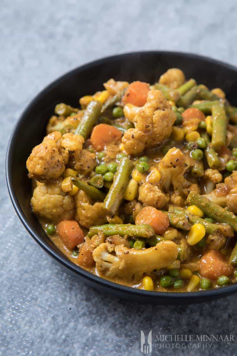 A bowl of vegetarian korma, cauliflower, green beans, corns in a orange sauce