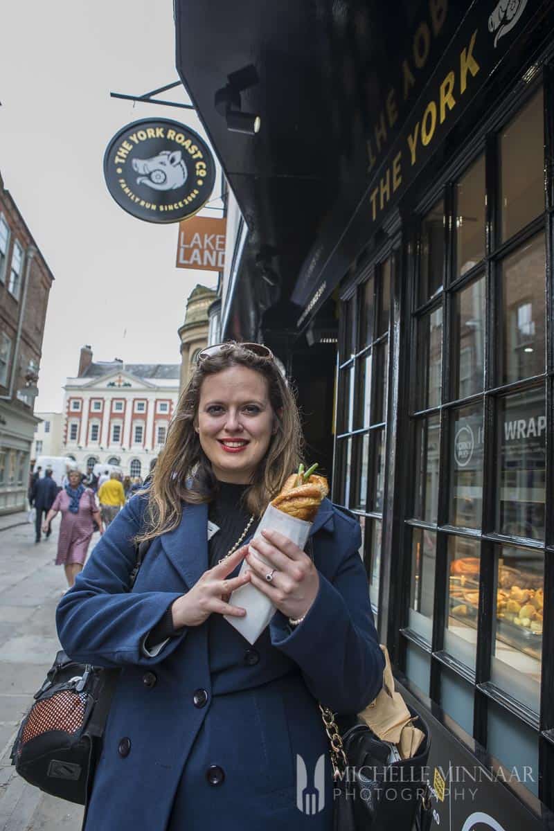 A woman in a blue jacket holding the sandwich outside the York Roast 