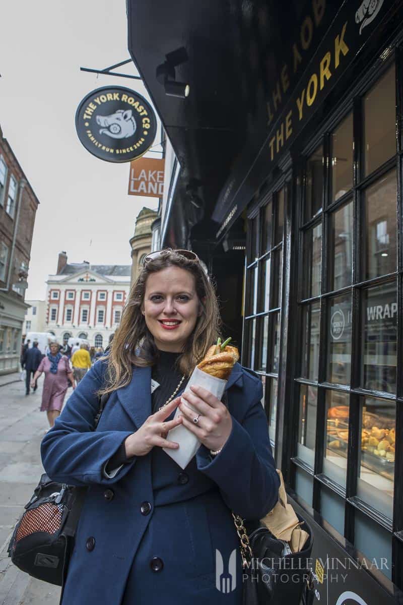 A woman in a blue jacket holding the sandwich outside the York Roast