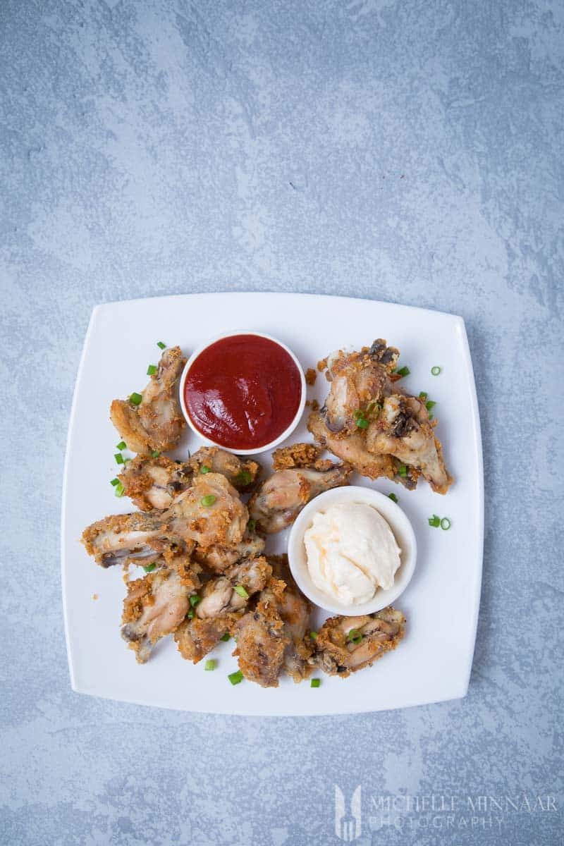 An aerial view of air fryer chicken wings on a plate with two small bowls of bbq sauce and mayo
