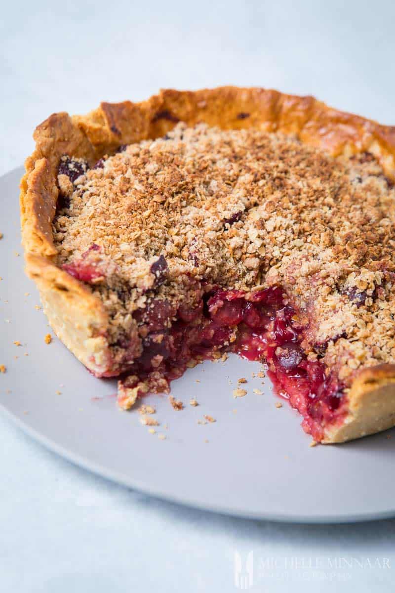 A close up of a cherry crumble pie with a slice taken out 