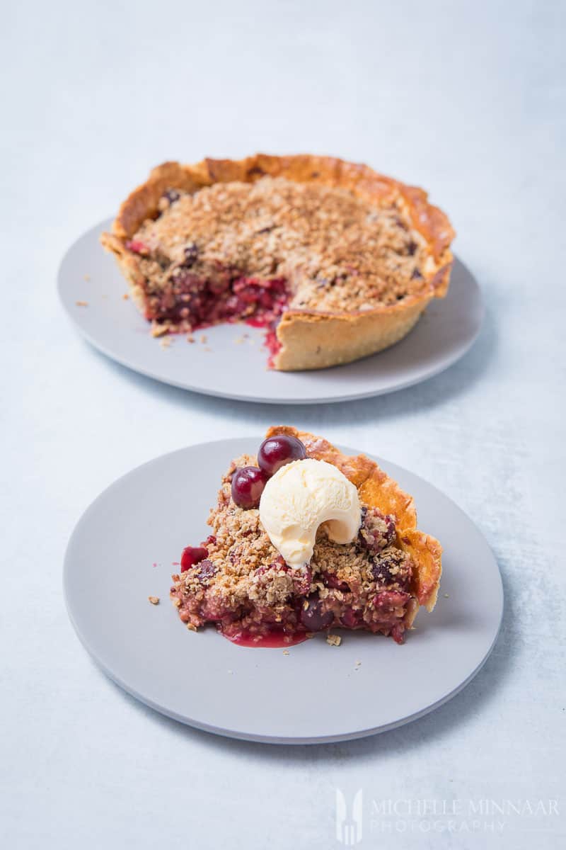 A Whole Cherry Crumble Pie and a slice taken out with a scoop of ice cream on top 