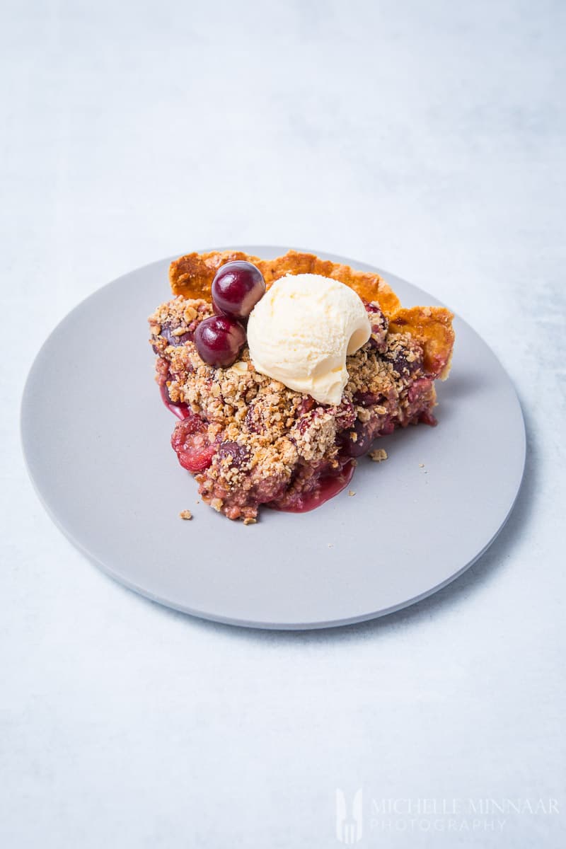 A slice of cherry crumble pie with ice cream on top
