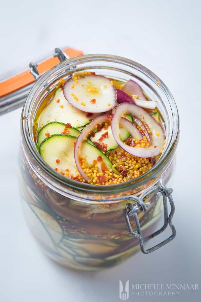 Courgette Pickle - an open glass gar with courgette, onions and spices 