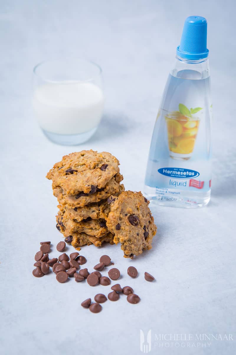 A bottle of Hermesetas liquid, a pile of sugar free chocolate chip cookies and a glass of milk 